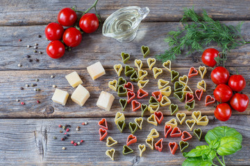 Naklejka na ściany i meble on a wooden background pasta in the form of hearts, tomatoes, basil, olive oil, dill, pepper, cheese