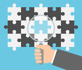 Searching for the missing puzzle concept. Hand holding magnifying glass over a puzzle pattern