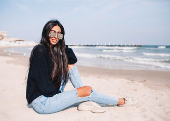 She is simply gorgeous. Beautiful young woman posing and looking away with smile while sitting on the beach.Portrait of a young and cute Chinese Asian woman.
