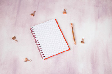 on a pink background notepad, paper clips, pen in rose gold