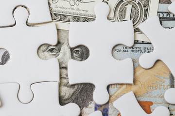 Solving the financial or business problem or idea for making money concept, white jigsaw puzzle game on US Dollar banknote with the eyes of Ben Franklin face