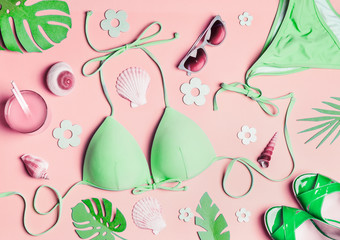 Summer flat lay. Green woman's beach accessories: swimsuit bikini , sandals, drink, sunglasses , sea shells and tropical leaves on pink background, top view. Summer holiday concept. Tropical vacation
