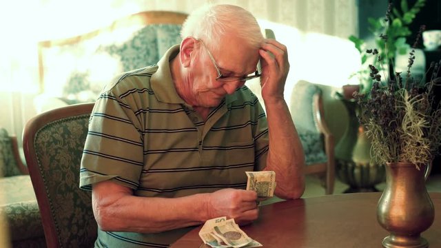 Sad, senior man counting bills by table at home, 4K