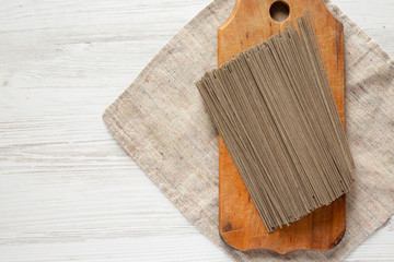 Fototapeta premium Dried buckwheat soba noodles on rustic wooden board over white wooden background, top view. Copy space.