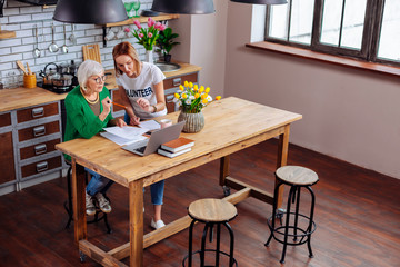 Social employee showing grey-haired dame presentation about loans on laptop