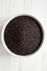 Gluten free raw organic black quinoa in a bowl over white wooden surface, top view. From above, overhead, flat lay. Closeup.