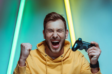  handsome and screaming man looking at camera and holding gamepad - obrazy, fototapety, plakaty