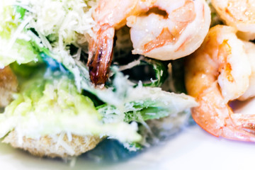 Caesar salad with shrimps on white plate in restaurant.
