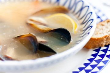 Seafood soup with mussels, prawns and fish in white bowl with blue ornament in restaurant.