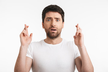Image of shocked man 30s with bristle in casual t-shirt keeping fingers crossed and making a wish