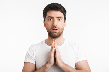 Image of concentrated man 30s with bristle in casual t-shirt holding palms together and praying