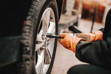 Close up of auto mechanic using wrench and changing tire in workshop.