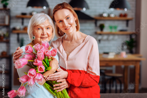 Attractive daughter posing with silver-haired mother with tulips bouquet