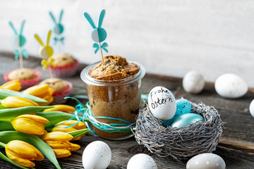 Osternest mit Eiern, Kuchen und Tulpen auf altem Holz