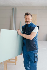 Worker carrying gypsum plasterboard indoors