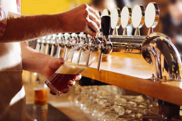 Barman wearing beige apron pouring beer for his client