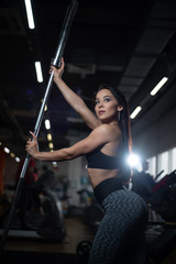 Fototapeta na wymiar Girl posing in the gym, showing off her body, holding a barbell