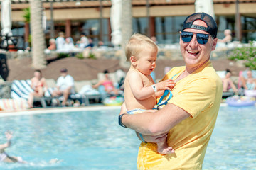 Obraz na płótnie Canvas Happy father spending time with his baby son by the pool in the resort.