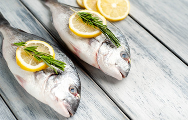 Two fresh raw Dorado fish with spices and olive oil on a wooden table.