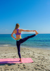 Woman training yoga on the beach. Girl is wearing sportive clothes doing sport on mat on the sea beach. Caucasian female practicing fitness, pilates and meditation. 