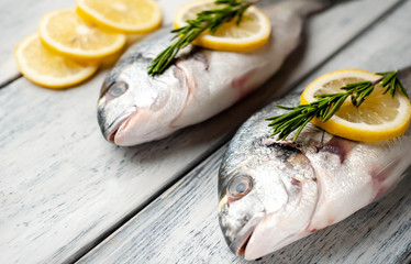 Two fresh raw Dorado fish with spices and olive oil on a wooden table.
