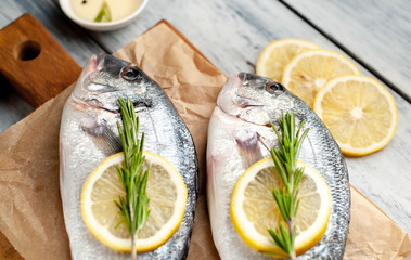 Two fresh raw Dorado fish on a cutting board with spices and olive oil on a wooden table