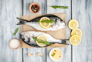 Two fresh raw Dorado fish with spices and olive oil on a wooden table.