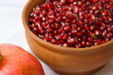 whole ripe pomegranate, pomegranate grains in a brown ceramic plate on a white fabric background, close up