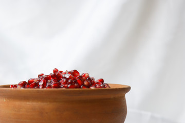 whole ripe pomegranate, pomegranate grains in a brown ceramic plate on a white fabric background, close up