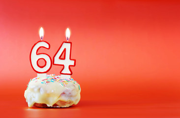 Sixty four years birthday. Cupcake with white burning candle in the form of number 64. Vivid red background with copy space