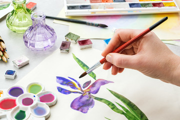 Iris flower and artistic equipment on desk. Top view. Painter drawing at working place.