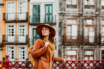 .Young and pretty woman wearing brown hat sightseeing in the city of Porto, Portugal. Standing around the all city with colored facades at background. Lifestyle.