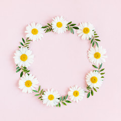 Round frame, wreath made of chamomiles, petals, leaves on beige background. Flat lay, top view