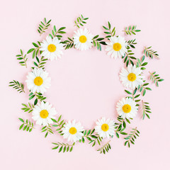 Round frame, wreath made of chamomiles, petals, leaves on beige background. Flat lay, top view