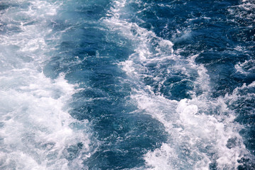 Turbulence made by foam of sea water from a high-speed yacht on surface of sea. Blue sea waves with lot of sea foam. Surface of sea with waves, splash, foam and bubbles, blue background and wallpaper.
