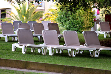 Exotic beach on mediterranean sea, sunbeds for sunbathing and relax on grass in tropical garden of luxury resort hotel. Sun loungers on lawn waiting for tourists. Idyllic seaside in summer season.