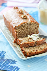 Banana bread or cake healthy and tasty breakfast. Loaf with walnuts, icing and cream cheese. Pink and blue towel background. Selective focus.