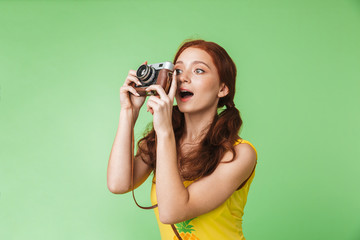 Happy young redhead girl photographer posing isolated over green wall background holding camera.