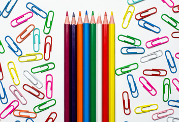 Many multi-colored stationery clips for documents and multi-colored pencils lie on a white background