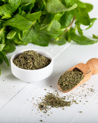 Dried peppermint in a white bowl and a bunch of fresh mint, on wooden background. Food background.
