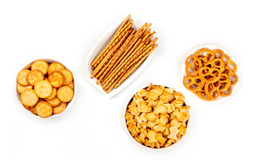 Salty crackers, sticks, pretzels, and goldfishes, shot from the top on a white background with copy space. Party snacks mix with a place for text