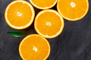 Many orange halves and a green leaf, shot from the top on a black background with a place for text