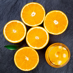 A glass of fresh orange juice with orange halves and a green leaf, shot from above on a black background