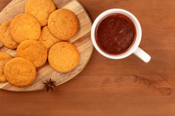 A closeup of ginger cookies, shot from above with a cup of hot chocolate and an anise star on a dark rustic wooden background with copy space