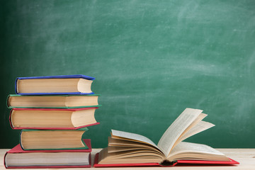 Education and reading concept - group of colorful books on the wooden table in the classroom, blackboard background