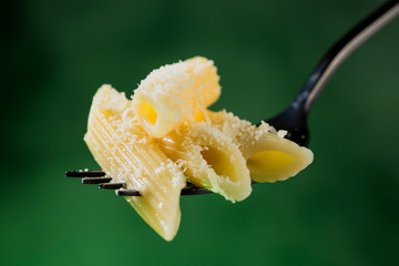 Pasta penne rigate on a fork sprinkled with grated cheese on a beautiful colored background....