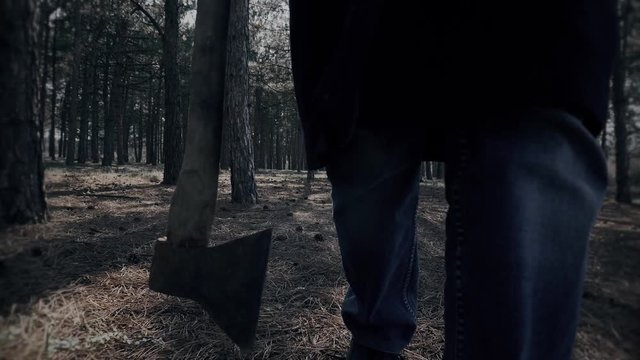 Mentally ill man walking with axe in woods in close up