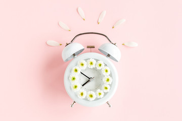 Composition-summer time from clock and chamomile flowers on pink background. Flat lay, top view 