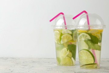 Mojito cocktail in a plastic glass with lime, mint and lemon on a light concrete table. make a mojito.