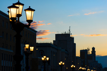 Fototapeta na wymiar Lamp posts at seafront and promenade in Bari, Italy. Romantic, calm, relaxing evening in city. Sun is setting over old town.